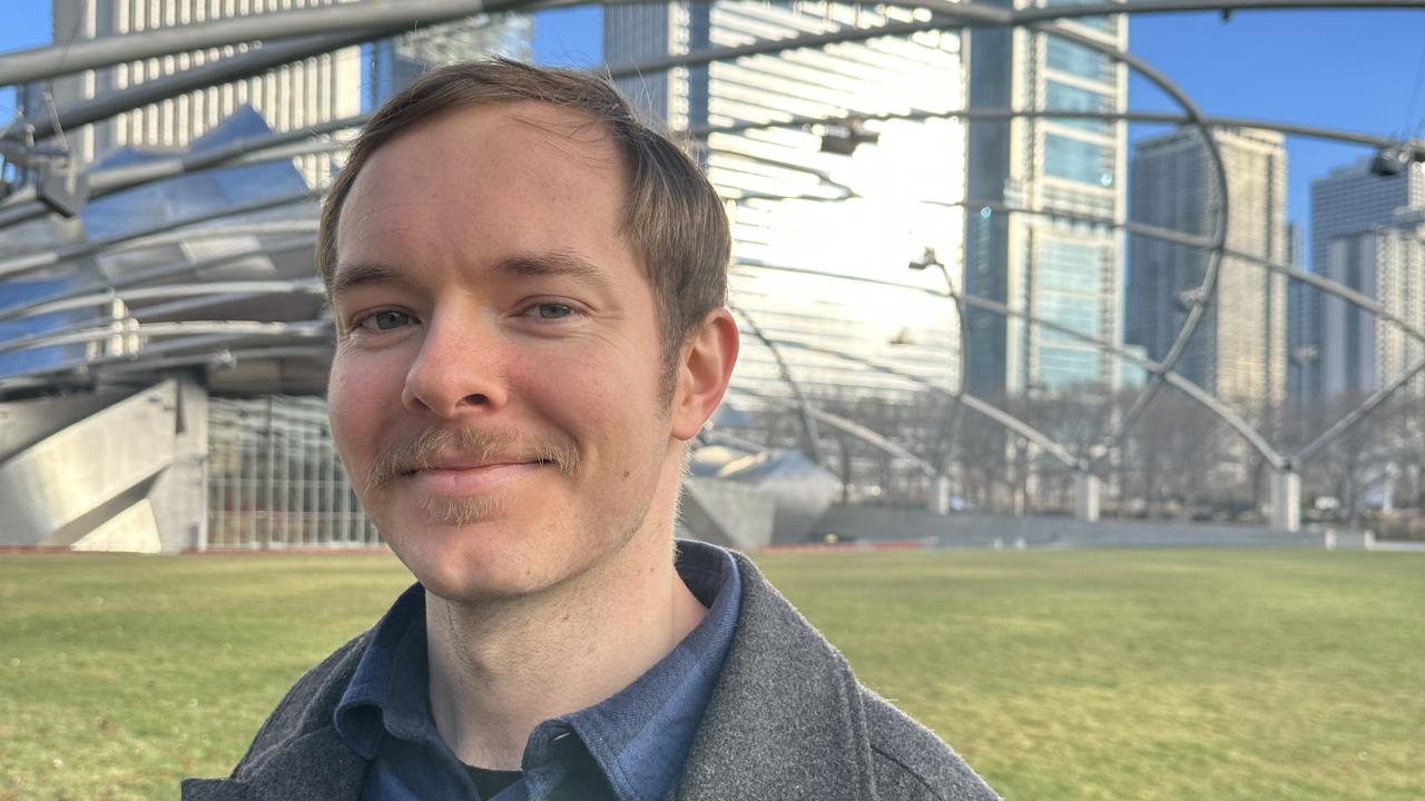 Isaac Neal stands on a grassy lawn with large skyscapers in the near background.