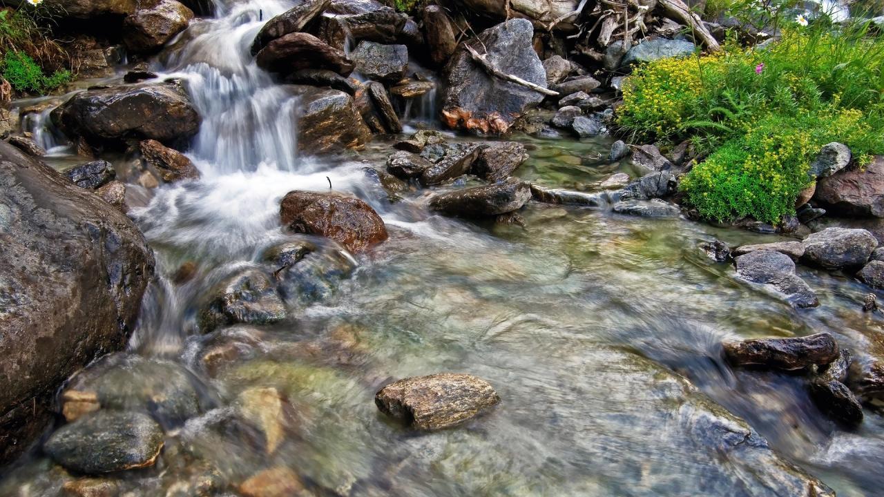 A time-lapse photo showing water from a small stream cascading around several medium to small rocks.
