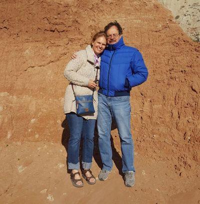 Couple smiling with arms around each other beside a red sandstone cliff